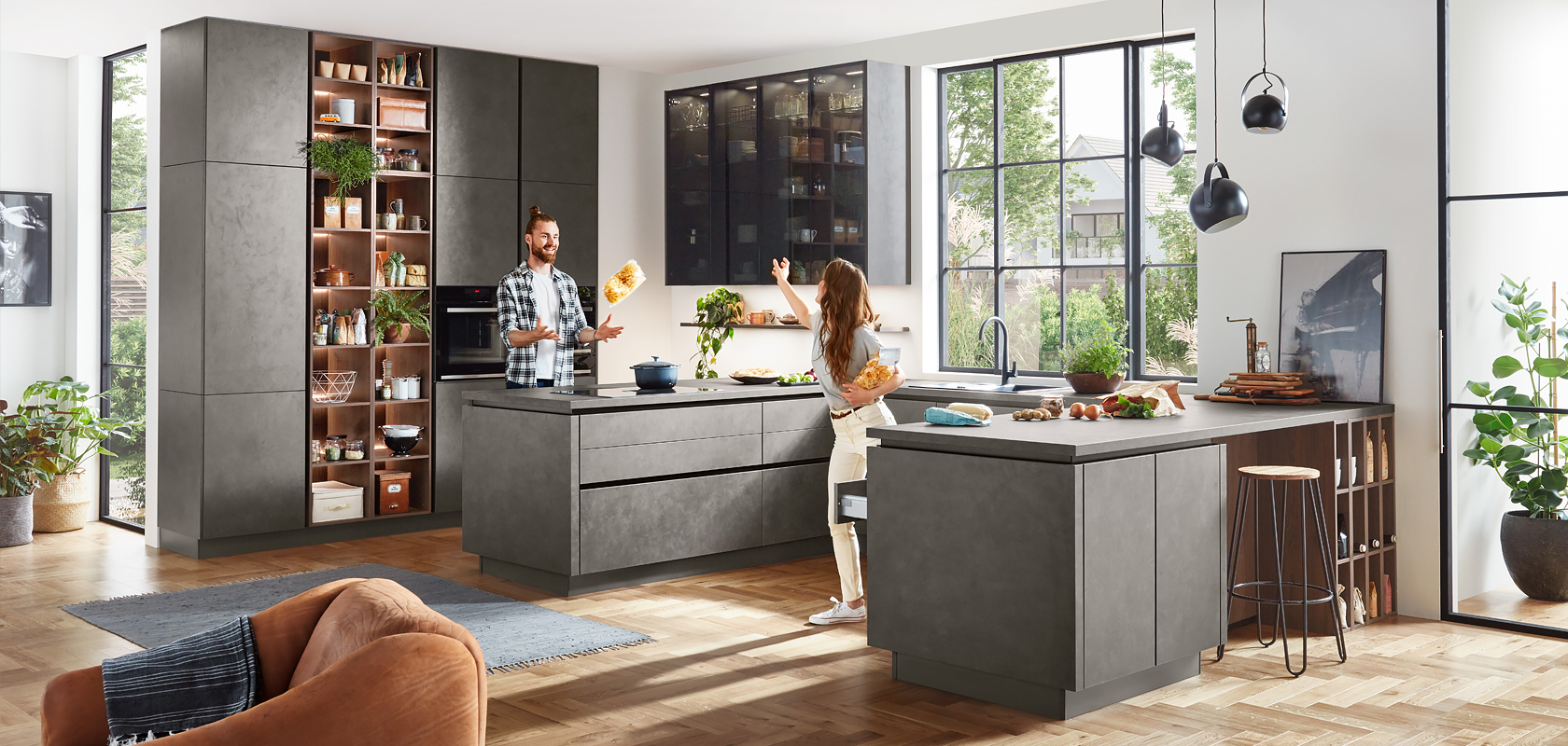 Design moderno della cucina con mobili grigi eleganti, elettrodomestici integrati e un'isola centrale. Una coppia si diverte a cucinare nell'ambiente ben illuminato e spazioso.