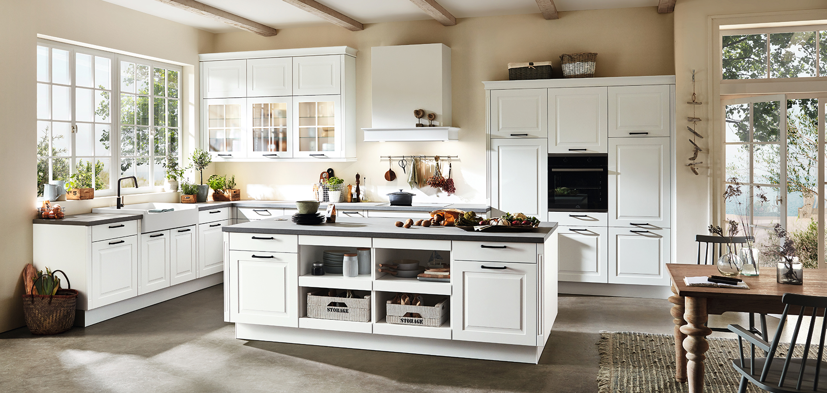 Amplio interior de cocina con gabinetes blancos, encimeras negras, electrodomésticos modernos y una isla central bañada por luz natural de grandes ventanas.