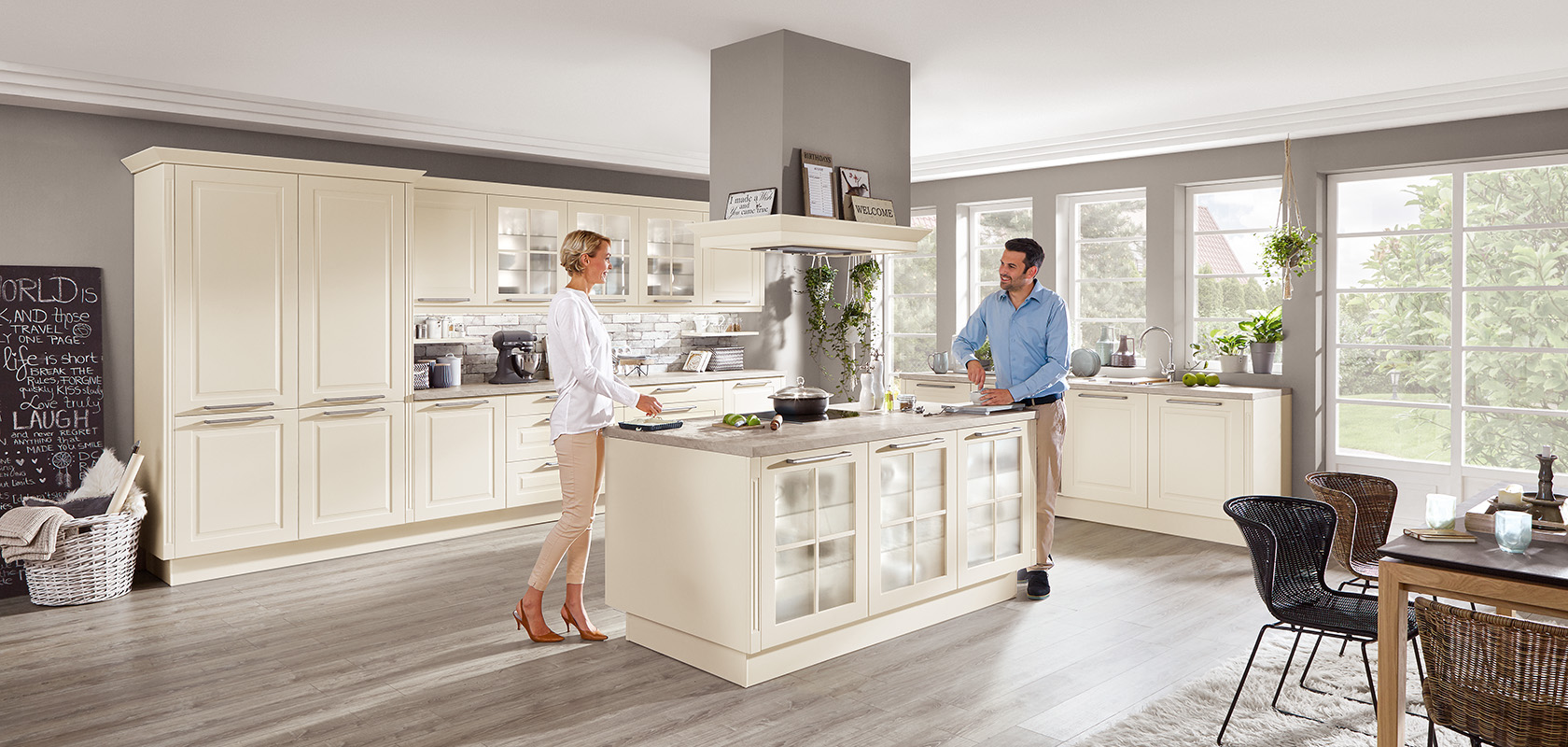 A bright, spacious kitchen with classic cabinetry and a central island, with two individuals engaged in cheerful conversation amidst meal preparation.