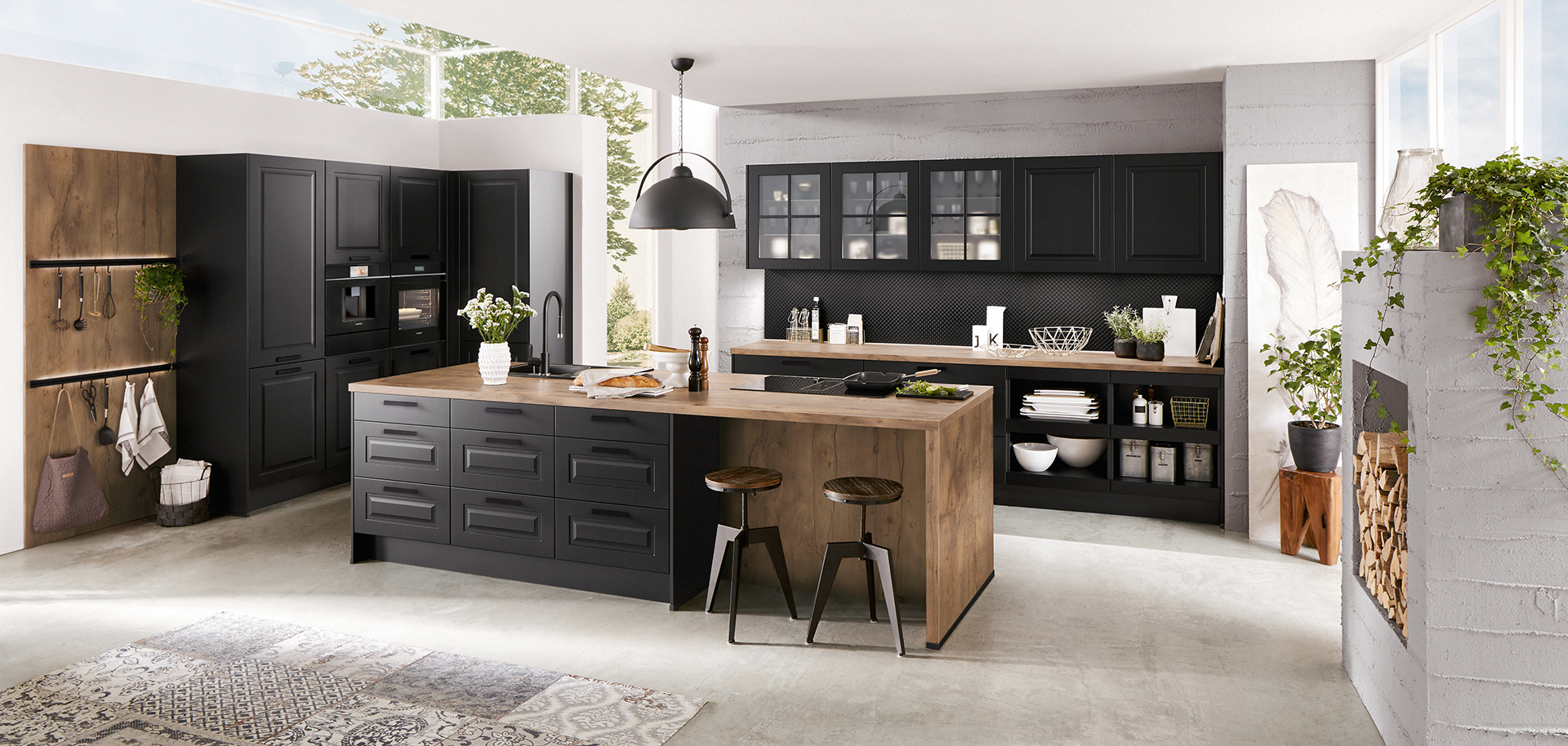 Interni di cucina moderna che mostrano eleganti armadi neri, dettagli in legno e un'isola centrale, arricchiti da luce naturale e verde per uno spazio elegante e accogliente.