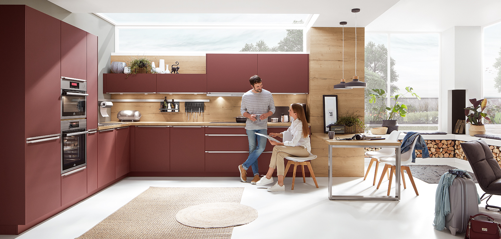 Modern kitchen with sleek maroon cabinets, stainless steel appliances, and wood accents, featuring a couple in casual attire having a pleasant conversation.