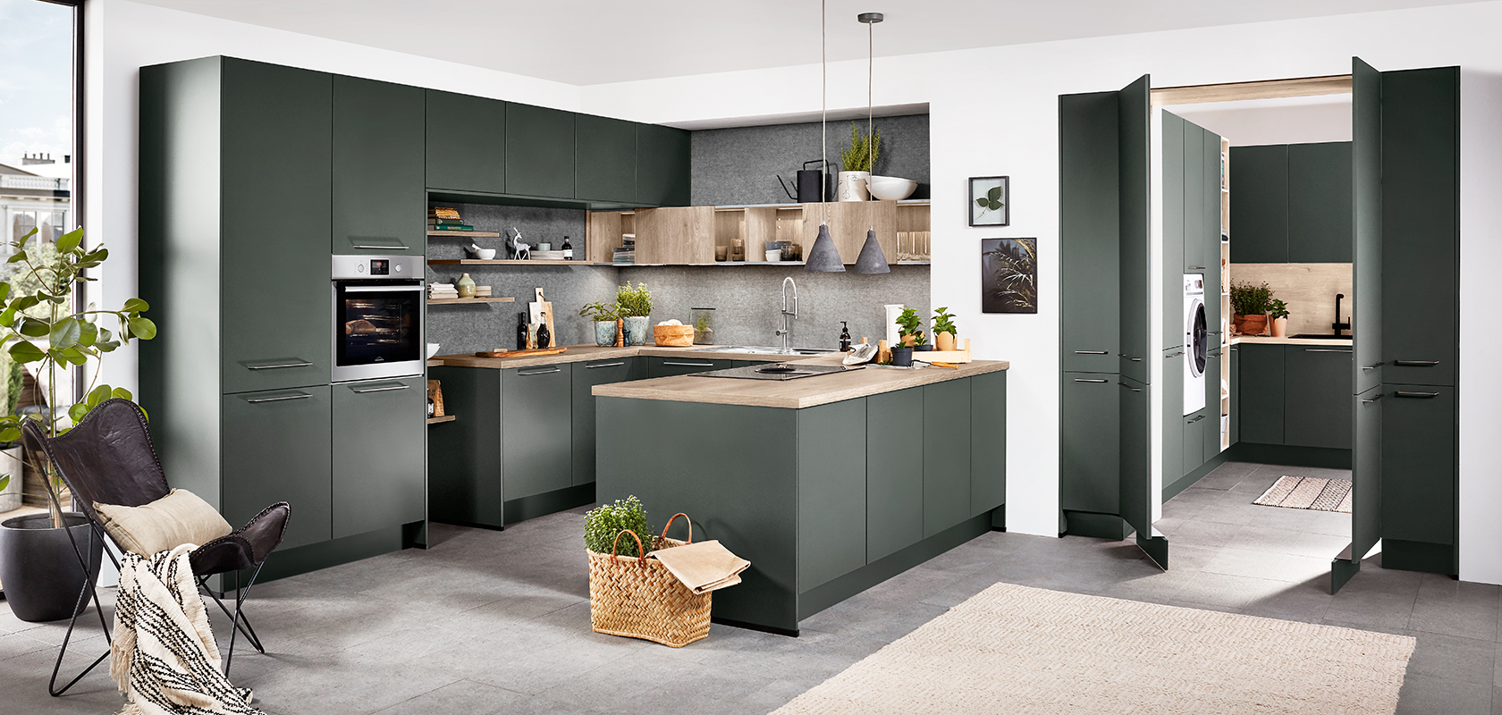 Modern kitchen with green cabinetry, wood accents, and stainless steel appliances, featuring a central island and well-lit, spacious design for a contemporary home.