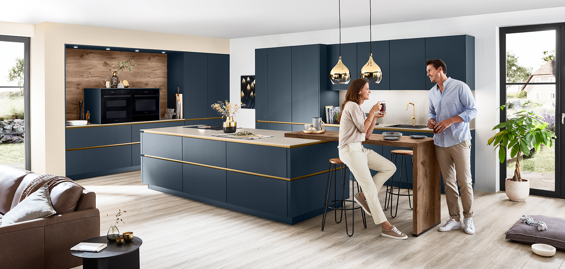 Modern kitchen interior with a couple enjoying wine around a stylish island with sleek navy cabinetry and elegant gold trim, under warm pendant lights.