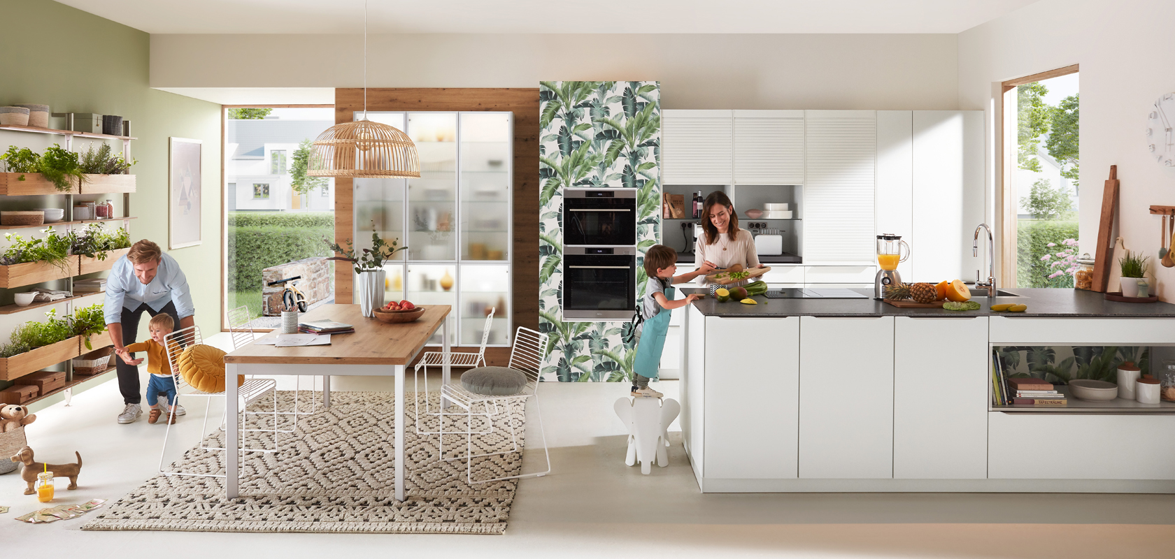 Moderní kuchyňská scéna s rodinou; osoba vařící, dítě hrající si s psem a další osoba pracující u stolu, ukazující živé domácí prostředí.