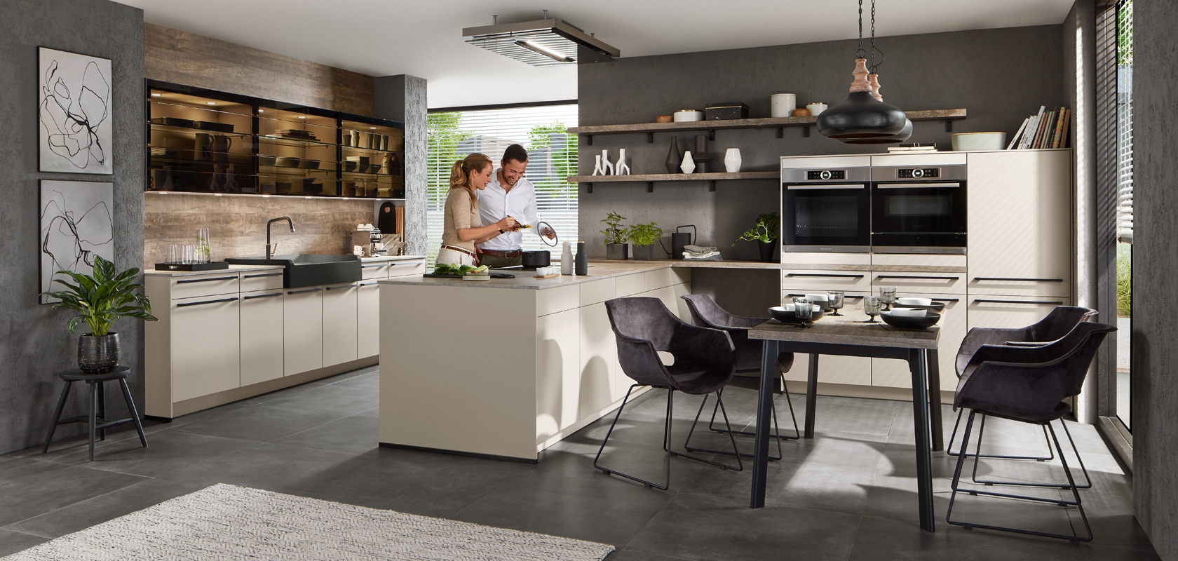 A modern, stylish kitchen with a couple cooking together, featuring sleek cabinetry, stainless steel appliances, and a cozy dining area with potted plants.