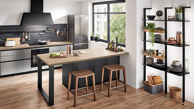 Moderne nobilia Küche mit Front Inox 216 und markanter schwarzer Dunstabzugshaube im Industrial-Stil. Die offene Raumgestaltung kombiniert Edelstahl-Optik mit warmem Holzdekor und funktionalem Regalsystem.