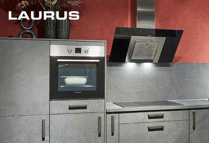 Moderní kuchyně předvádějící elegantní troubu LAURUS vestavěnou do tmavě šedého nábytku s nerezovými madly, pod černou odsavačkou par a proti červené zdi.