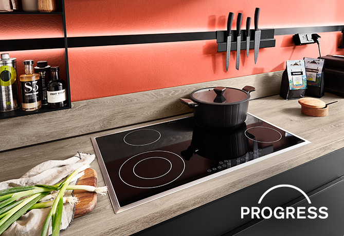 Moderní kuchyň s indukční varnou deskou s černým hrncem, obklopená elegantními pracovními plochami a stylově uspořádanými kuchyňskými náčiními a surovinami.
