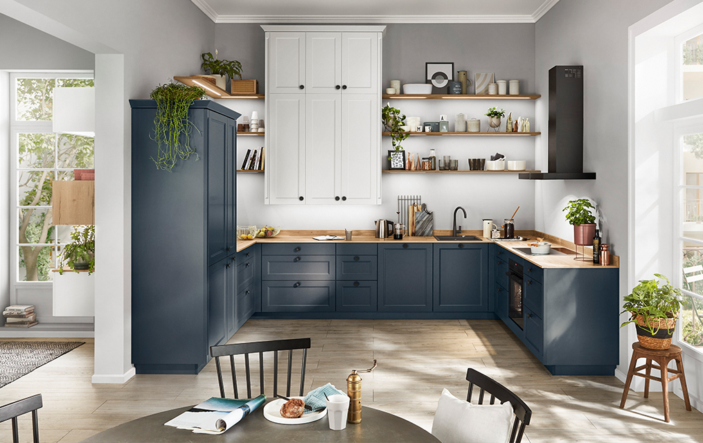 Současná kuchyně s modrými skříňkami, dřevěnými pulty a elegantními spotřebiči v prostorném, vzdušném prostoru s přirozeným světlem.