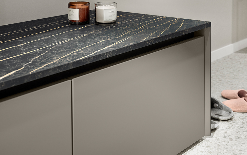 Elegant modern kitchen featuring a dark marble countertop with distinct veins atop sleek, gray cabinetry, complemented by two decorative candles and cozy house slippers.