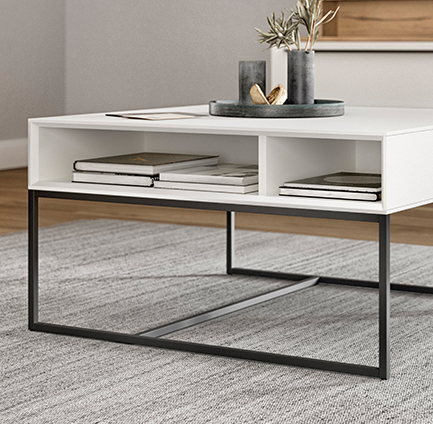 Minimalist white coffee table with sleek black metal legs, featuring an open shelf with books and decorative items, in a modern living space.