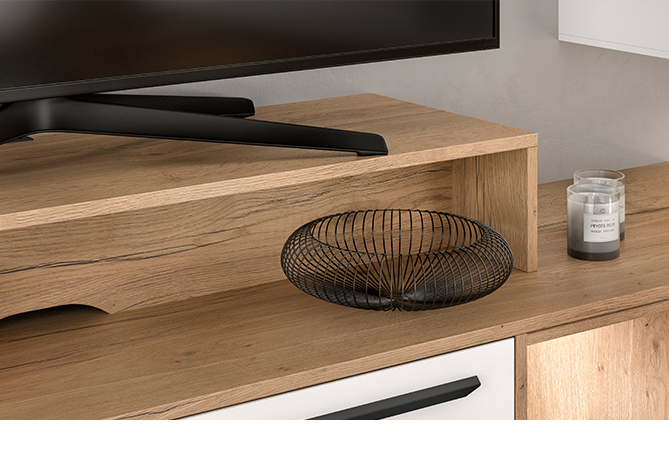 Escritorio de madera contemporáneo con un elegante monitor negro, un minimalista cuenco de frutas de metal y una pequeña vela aromática creando una estética de espacio de trabajo moderno y limpio.