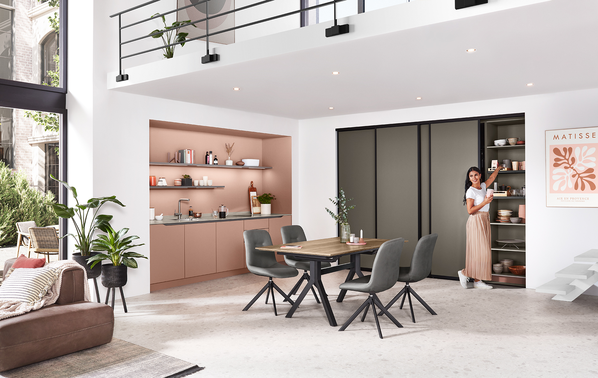 Modern kitchen and living area with an open-plan design, featuring clean lines, minimalist decor, and a welcoming hostess by the kitchen counter.