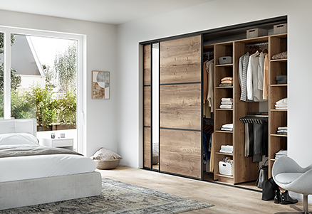 Dormitorio moderno con un gran armario corredero con compartimentos abiertos, mostrando una solución de almacenamiento ordenada y organizada en un espacio luminoso y naturalmente iluminado.