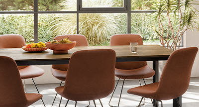 Elegant dining area featuring a sleek wooden table with terracotta chairs, natural light, and greenery enhancing a modern, serene home ambiance.