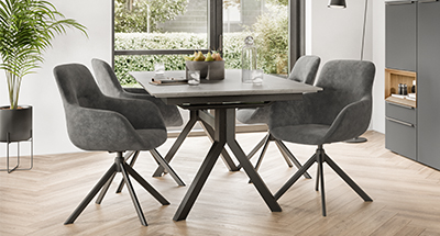 Moderní jídelna s elegantním stolem s tmavým dřevěným vrškem, unikátními kovovými nohami a čtyřmi plyšovými šedými židlemi v klidném prostředí.