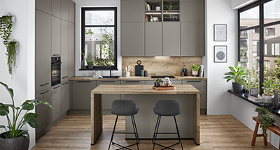 Moderní kuchyňský interiér s elegantními šedými skříněmi, dřevěnými doplňky a nerezovými spotřebiči, doplněný přírodním světlem a zelení.