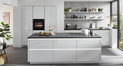 Současná kuchyně s bílými skříňkami, nerezovými spotřebiči, poličkami a minimalistickým designem.