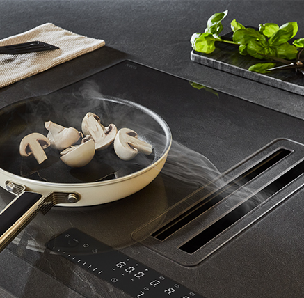 Elegant modern kitchen featuring an induction cooktop with a white pan cooking mushrooms, accompanied by fresh basil on a sleek dark countertop.