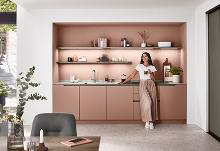 Una cocina moderna con líneas limpias que presenta a una mujer sonriente sosteniendo una taza de café, rodeada de gabinetes minimalistas y elegantes acentos decorativos.