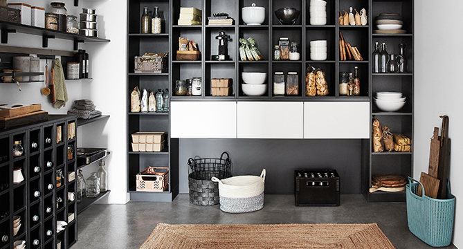 Elegancka, nowoczesna spiżarnia kuchenna z czarnymi półkami, starannie zorganizowanymi pojemnikami, koszami, przyprawami i narzędziami, tworząca elegancką i funkcjonalną przestrzeń do przechowywania.