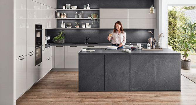 Una cocina moderna con una mujer preparando comida en una isla elegante, rodeada de gabinetes elegantes y electrodomésticos de última generación.