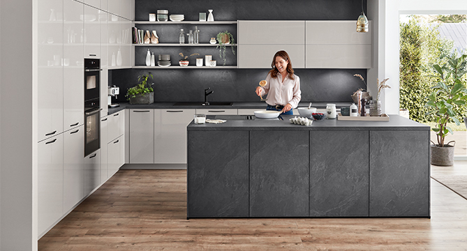 A modern kitchen with a woman preparing food on a sleek island, surrounded by stylish cabinetry and state-of-the-art appliances.