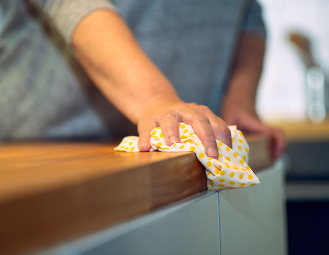 Osoba utírající kuchyňský pult žlutým vzorovaným hadříkem, zaměřená na čistotu a údržbu domácnosti.
