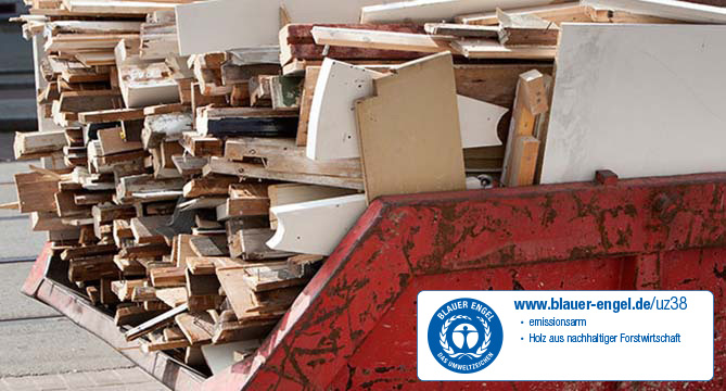 Un montón de tablas de madera variadas y piezas de muebles viejos arrojados en un contenedor grande de color rojo, indicando una limpieza de construcción o renovación.