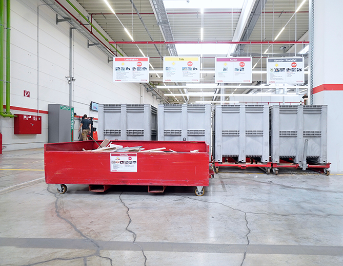 A clean, organized industrial space with lined-up waste disposal bins and a red dumpster in the foreground, indicative of efficient waste management practices.