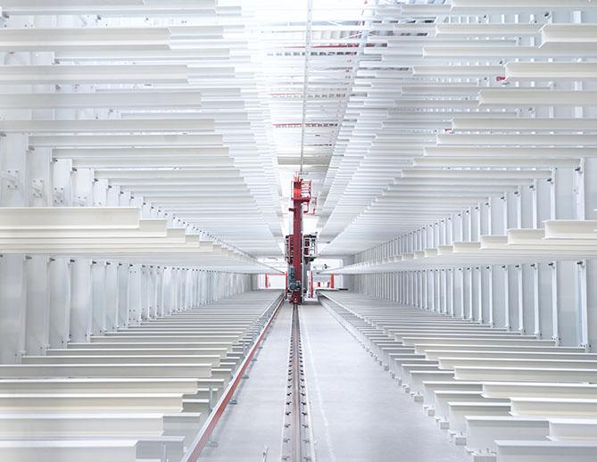 Modern automated warehouse with white metal shelves and a red robotic picking system operating along the narrow corridor between racks.