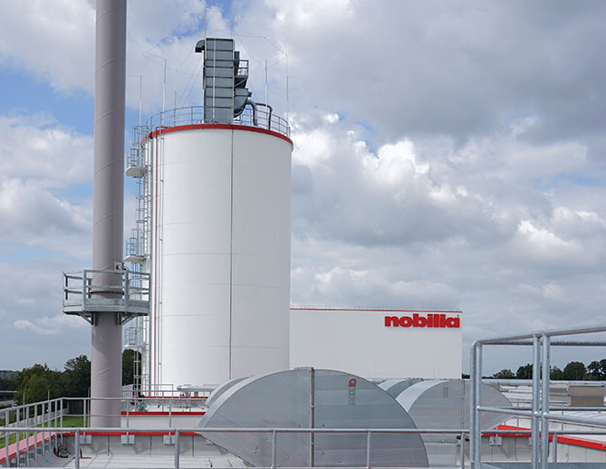 Installation industrielle avec des réservoirs de stockage, des structures métalliques et des pipelines sous un ciel nuageux, mettant en valeur l'infrastructure d'une usine de fabrication moderne.