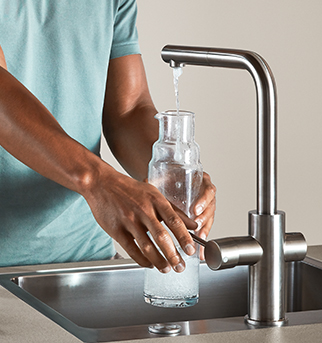 Una persona riempie una bottiglia di vetro trasparente con acqua da un rubinetto da cucina in acciaio inossidabile moderno, dimostrando facilità d'uso e accesso all'acqua pulita.