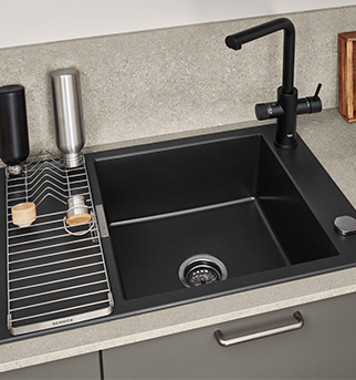 Moderní kuchyňský dřez s matně černou baterií a umyvadlem s pečlivě umístěnými doplňky, včetně dávkovače na mýdlo a pruhované utěrky.