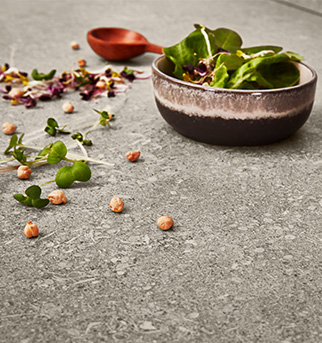 Hliněná keramická mísa naplněná čerstvou zeleninou na texturovaném povrchu, posypaná květinovými okvětními lístky, bylinkami a cizrny; vedle odpočívá měděná lžíce.