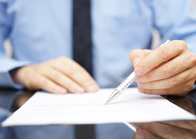 Eine professionelle Person in einem blauen Hemd und Krawatte unterzeichnet ein Dokument, was Geschäftsvereinbarungen, Professionalität und offizielle Angelegenheiten symbolisiert.