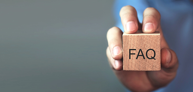 Hand holding a wooden block with "FAQ" lettering, symbolizing frequently asked questions or support information on a website.