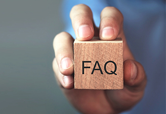 Eine Hand hält einen hölzernen Block mit dem Text "FAQ", was Kundensupport und häufig gestellte Fragen auf einer Website symbolisiert.